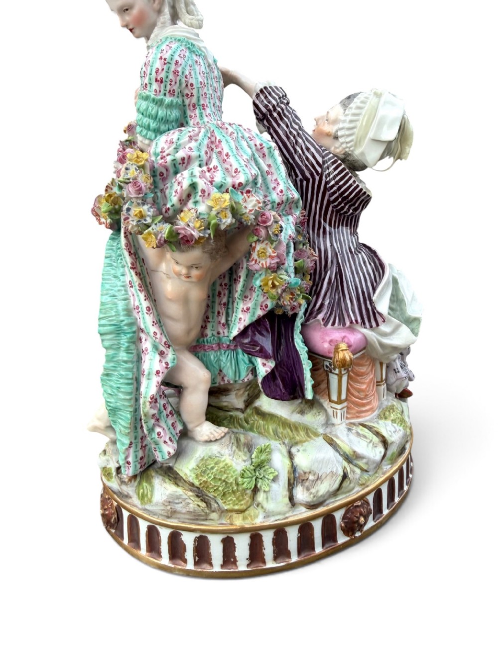 An eighteenth-century polychrome hard-paste porcelain figurine group depicting two classical figures and a cherub beside an overturned basket of eggs on a moulded fluted base. View XII