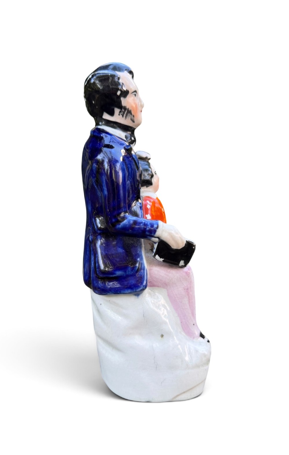 An antique Victorian Staffordshire earthenware figure depicting Lord Shaftesbury in a cobalt blue coat seated with a young child in an orange jacket on a white base. View II