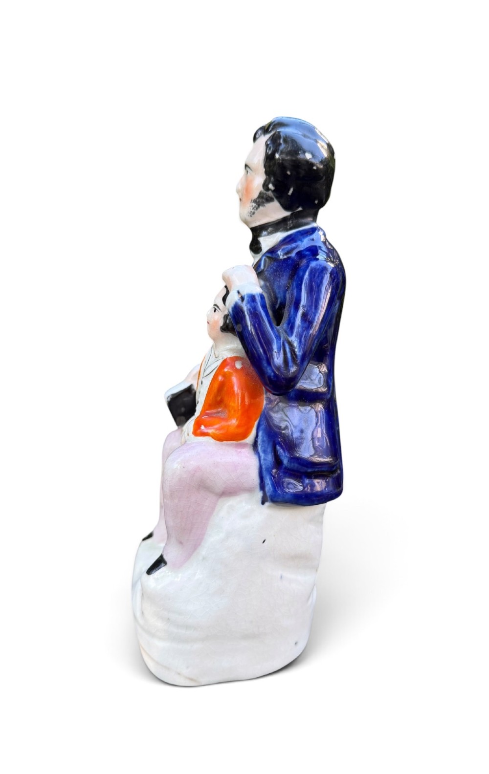 An antique Victorian Staffordshire earthenware figure depicting Lord Shaftesbury in a cobalt blue coat seated with a young child in an orange jacket on a white base. View IV
