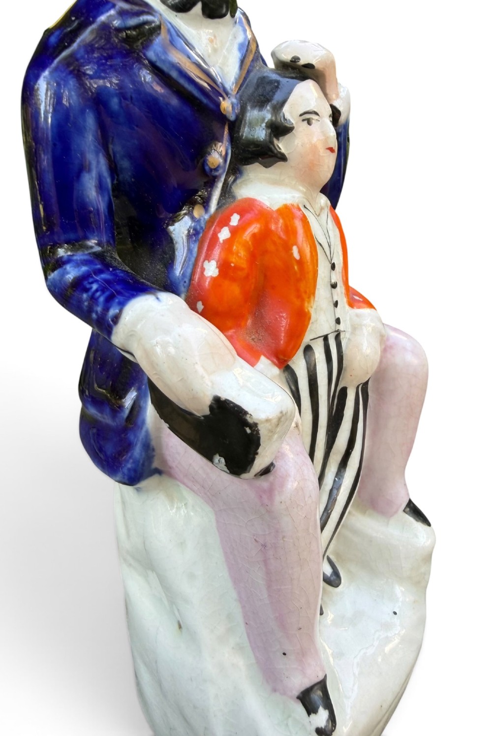 An antique Victorian Staffordshire earthenware figure depicting Lord Shaftesbury in a cobalt blue coat seated with a young child in an orange jacket on a white base. View VII