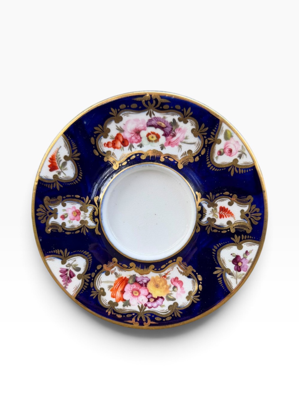 An antique Regency period Coalport porcelain cabinet cup and saucer featuring cobalt blue ground with gilt cartouches and hand-painted floral reserves. View II