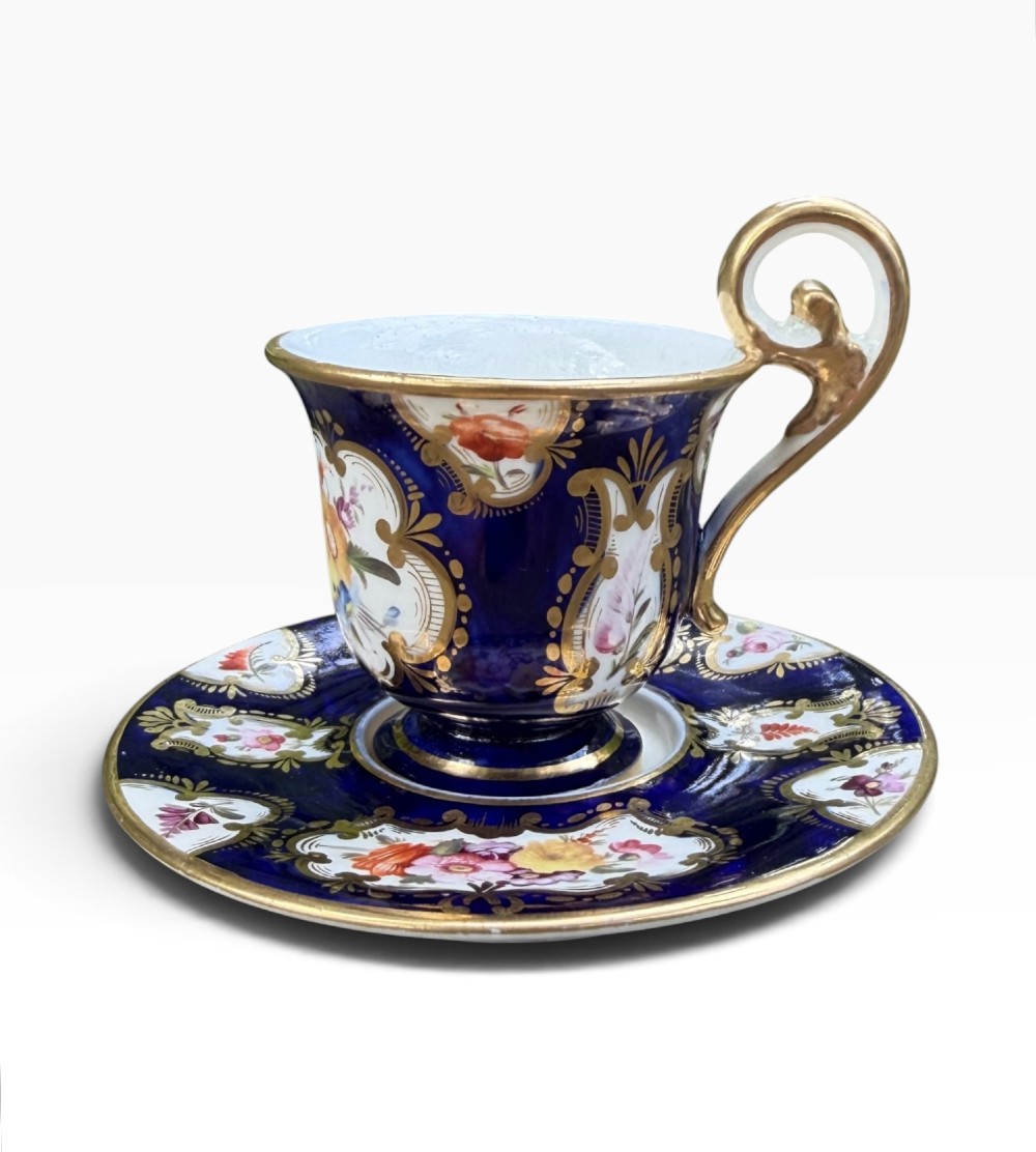 An antique Regency period Coalport porcelain cabinet cup and saucer featuring cobalt blue ground with gilt cartouches and hand-painted floral reserves. View V