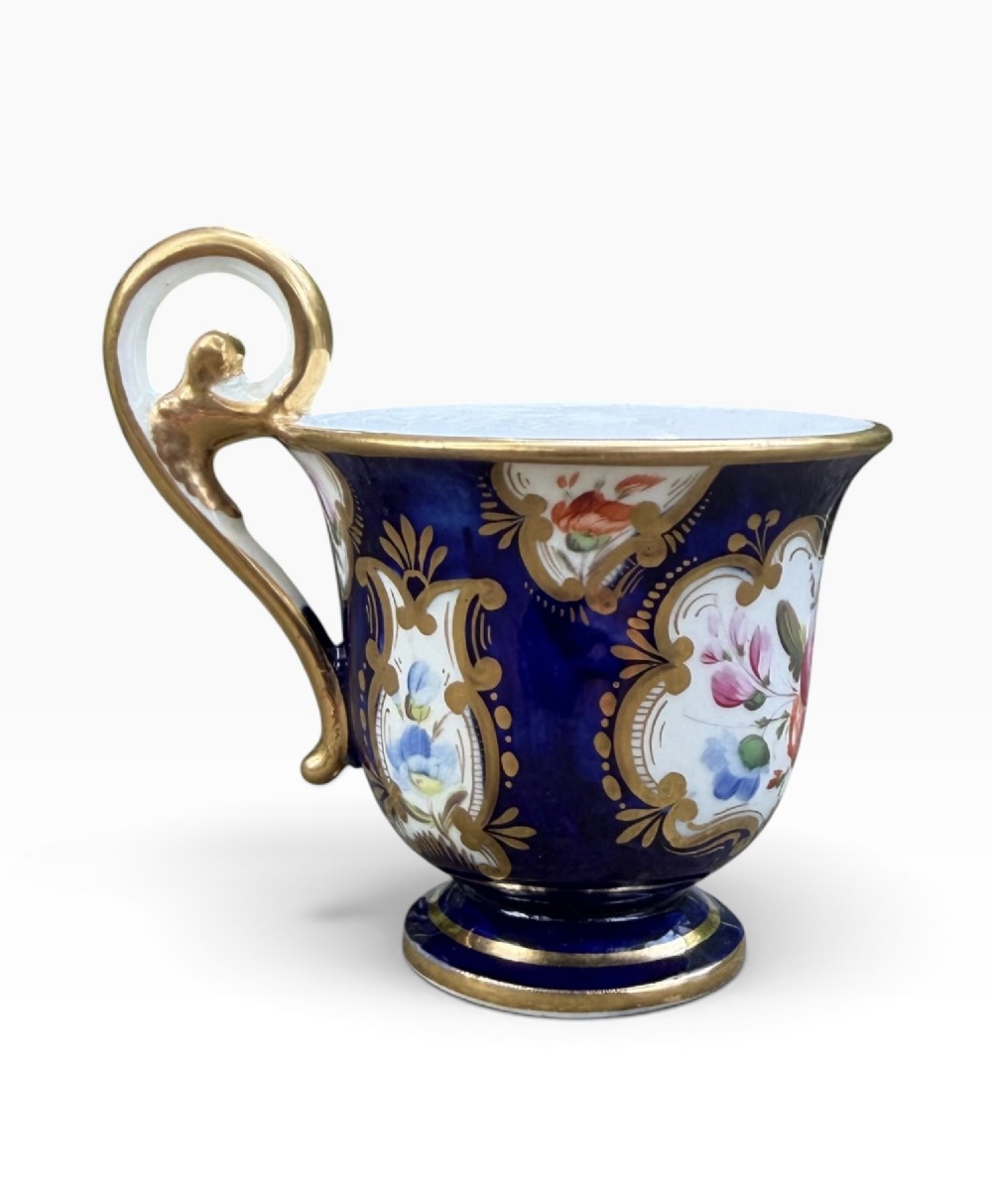An antique Regency period Coalport porcelain cabinet cup and saucer featuring cobalt blue ground with gilt cartouches and hand-painted floral reserves. View VII