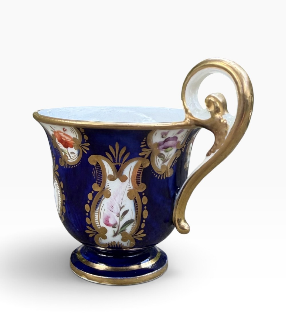 An antique Regency period Coalport porcelain cabinet cup and saucer featuring cobalt blue ground with gilt cartouches and hand-painted floral reserves. View IX