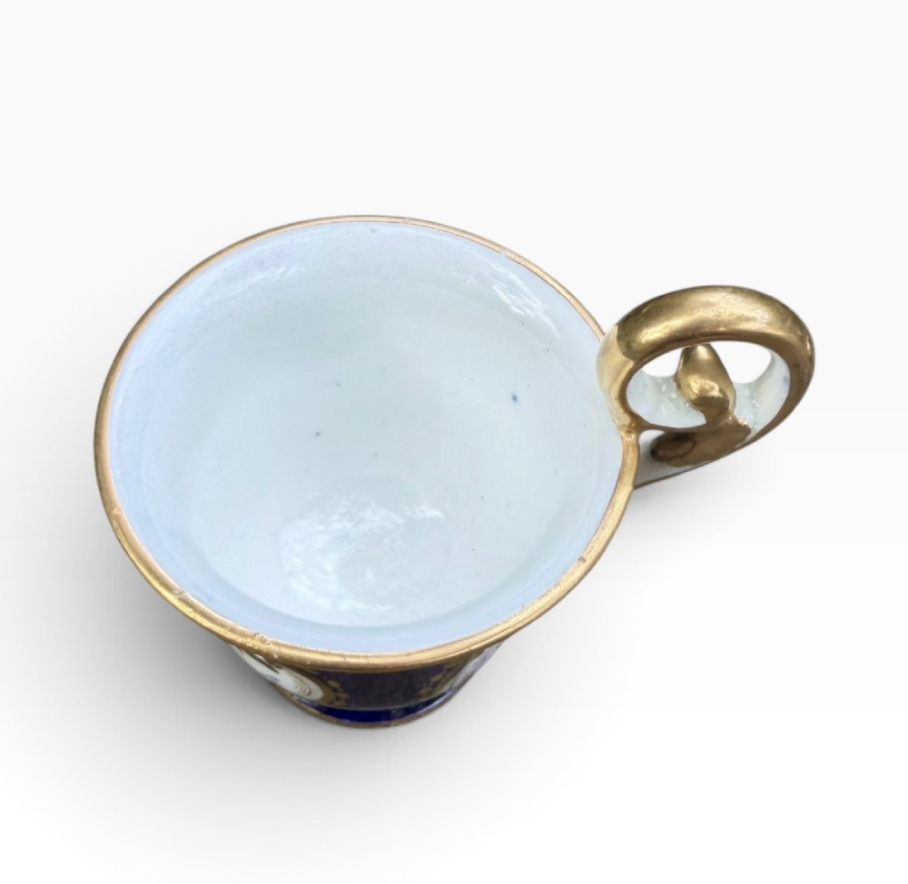 An antique Regency period Coalport porcelain cabinet cup and saucer featuring cobalt blue ground with gilt cartouches and hand-painted floral reserves. View X