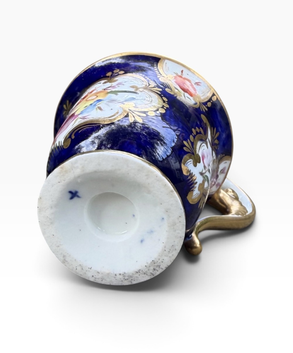 An antique Regency period Coalport porcelain cabinet cup and saucer featuring cobalt blue ground with gilt cartouches and hand-painted floral reserves. View XI
