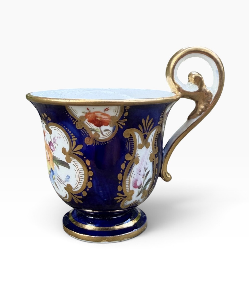 An antique Regency period Coalport porcelain cabinet cup and saucer featuring cobalt blue ground with gilt cartouches and hand-painted floral reserves. View XIII