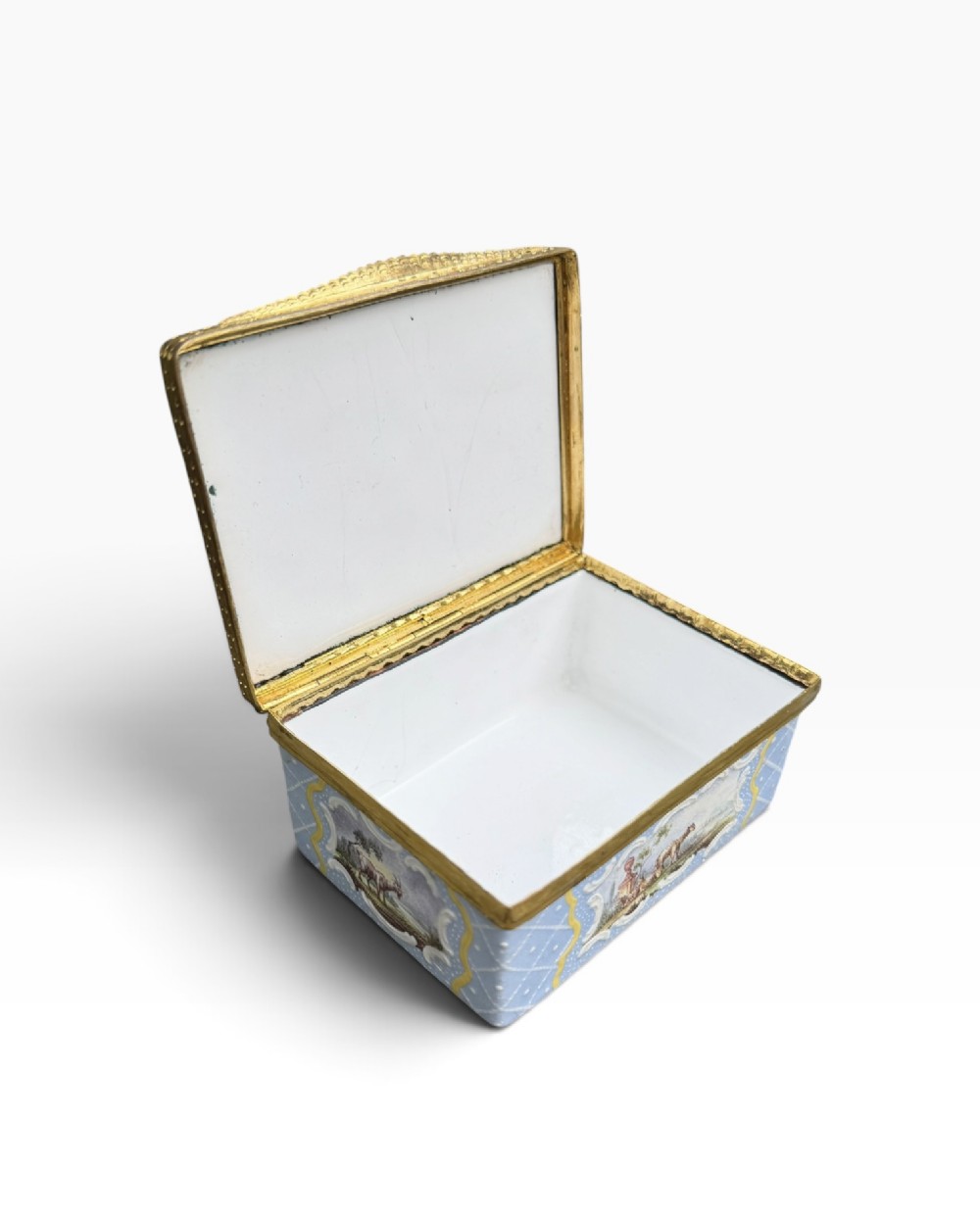 A rectangular Georgian enamel snuff box featuring a light blue trellis background, gilt metal mounts, and hand-painted pastoral scenes in central cartouches. View VII