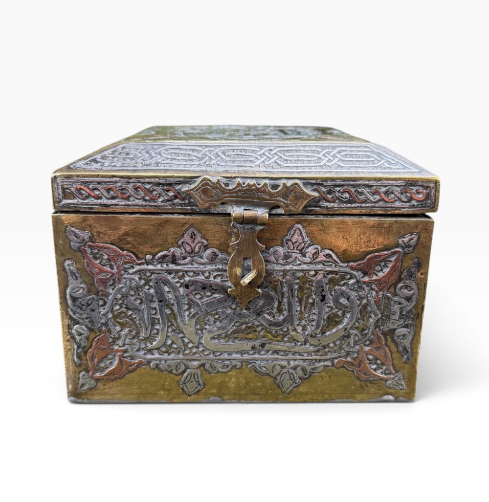 A square brass Quran casket featuring intricate silver and copper inlaid Arabic calligraphy and geometric interlace patterns. View II