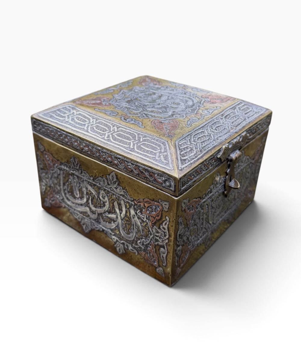 A square brass Quran casket featuring intricate silver and copper inlaid Arabic calligraphy and geometric interlace patterns. View V