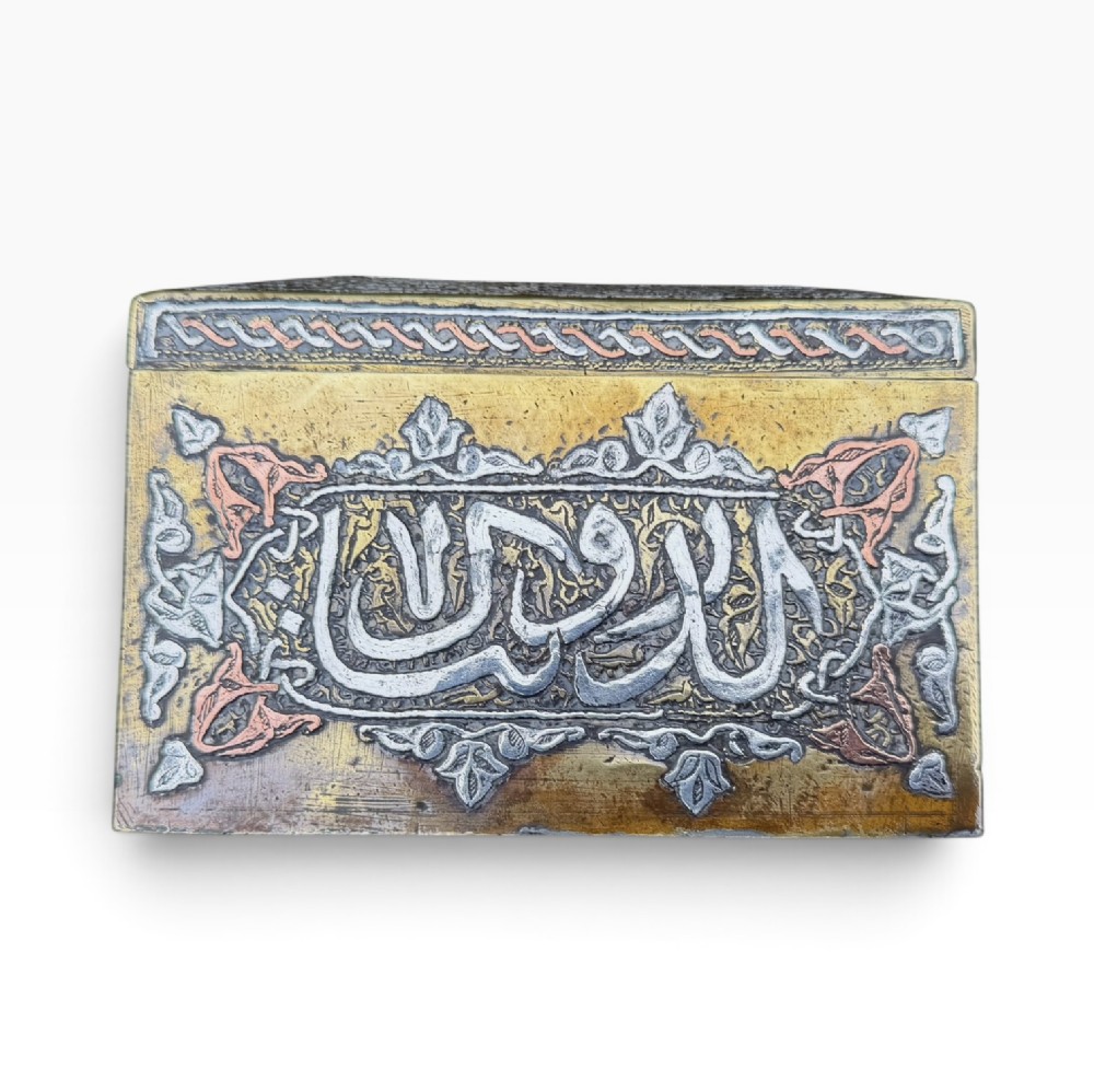 A square brass Quran casket featuring intricate silver and copper inlaid Arabic calligraphy and geometric interlace patterns. View IX