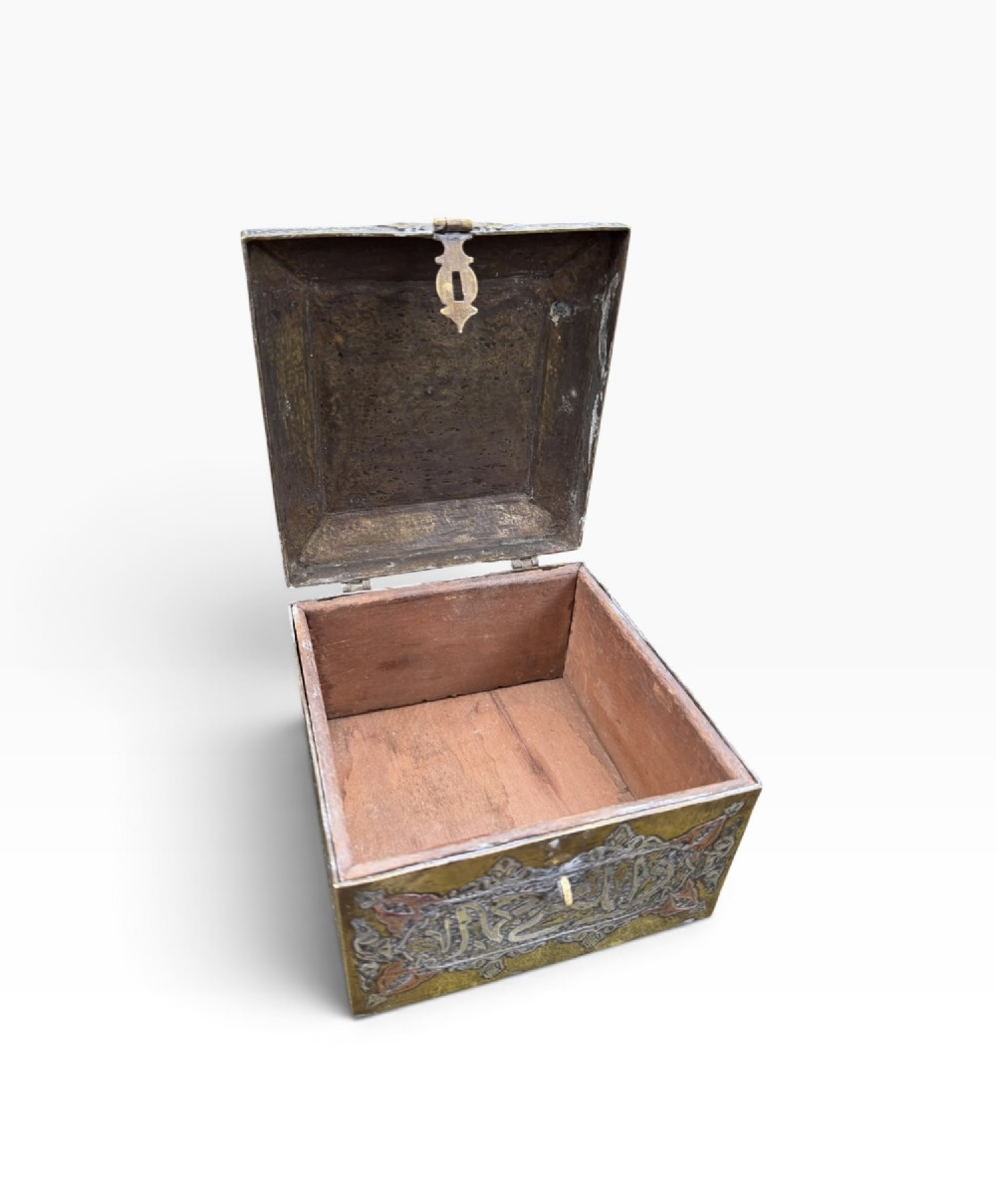 A square brass Quran casket featuring intricate silver and copper inlaid Arabic calligraphy and geometric interlace patterns. View X