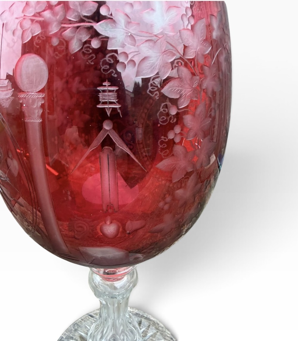 A Victorian cranberry glass goblet with intricately wheel-engraved Masonic symbols on a red bowl, supported by a clear knopped glass stem and a star-cut circular base. View VI