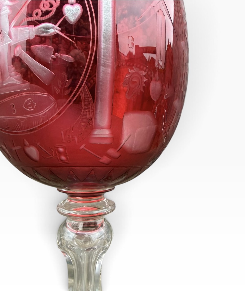 A Victorian cranberry glass goblet with intricately wheel-engraved Masonic symbols on a red bowl, supported by a clear knopped glass stem and a star-cut circular base. View VII