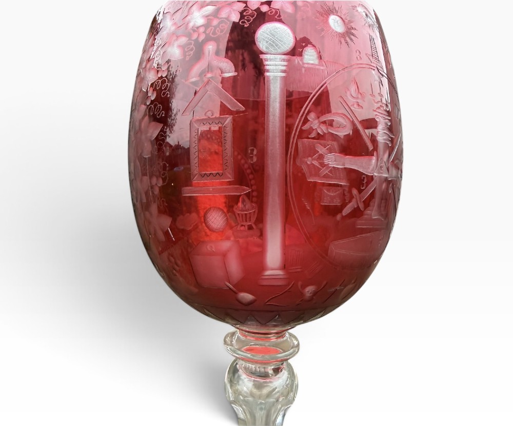 A Victorian cranberry glass goblet with intricately wheel-engraved Masonic symbols on a red bowl, supported by a clear knopped glass stem and a star-cut circular base. View VIII