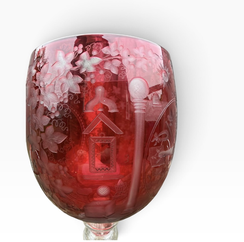 A Victorian cranberry glass goblet with intricately wheel-engraved Masonic symbols on a red bowl, supported by a clear knopped glass stem and a star-cut circular base. View IX
