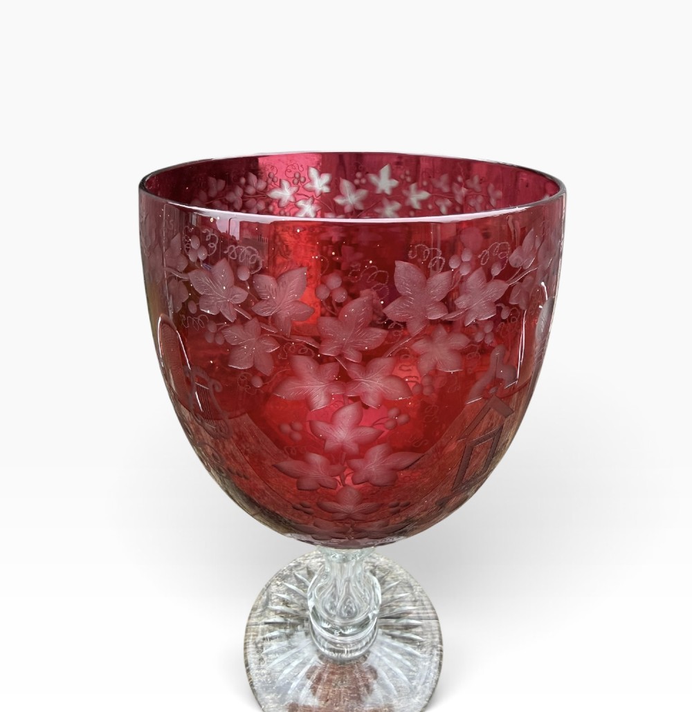 A Victorian cranberry glass goblet with intricately wheel-engraved Masonic symbols on a red bowl, supported by a clear knopped glass stem and a star-cut circular base. View X