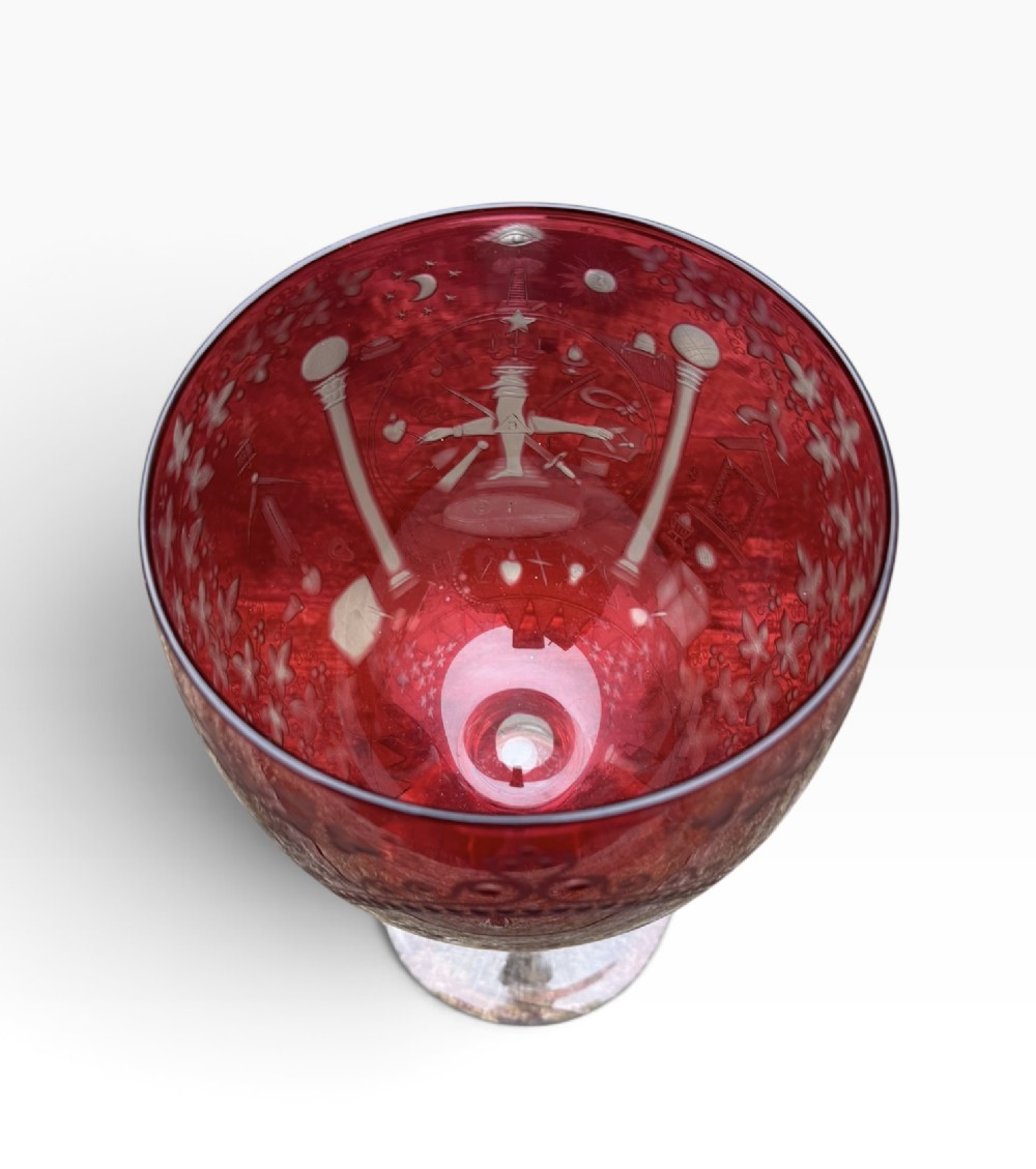 A Victorian cranberry glass goblet with intricately wheel-engraved Masonic symbols on a red bowl, supported by a clear knopped glass stem and a star-cut circular base. View XIII