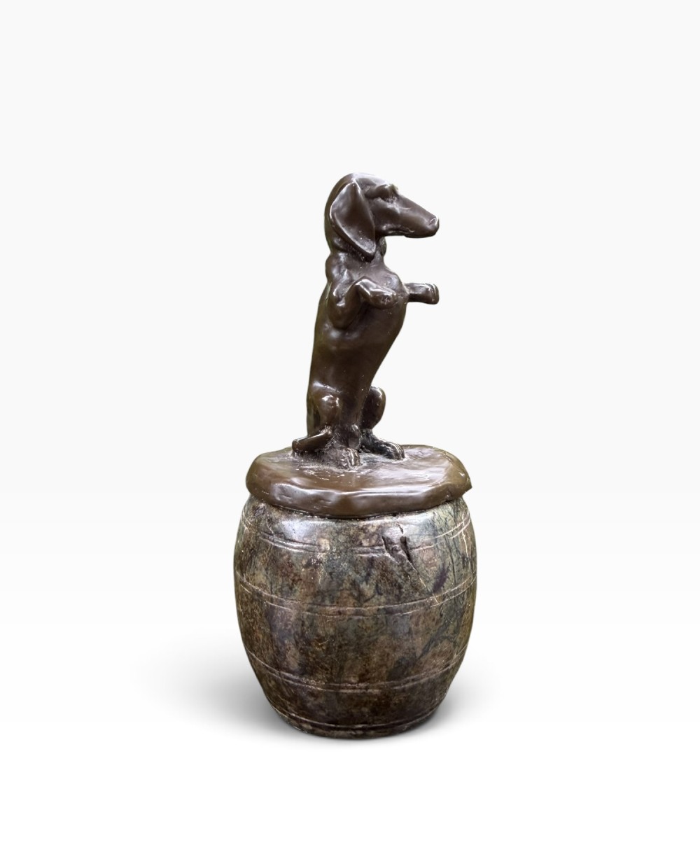 A small dark bronze sculpture of a dachshund standing on its hind legs in a begging position, mounted atop a carved marble barrel base.