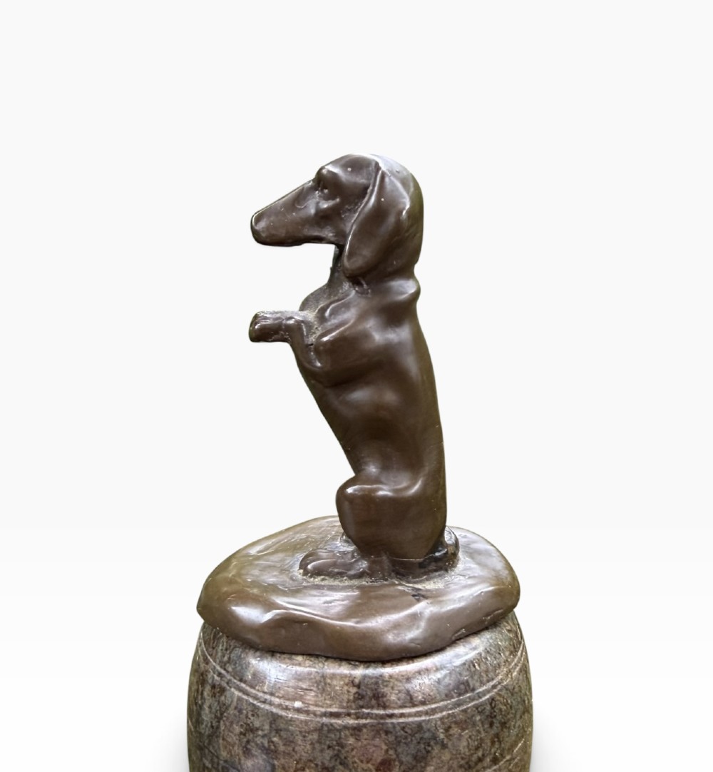 A small dark bronze sculpture of a dachshund standing on its hind legs in a begging position, mounted atop a carved marble barrel base. View III