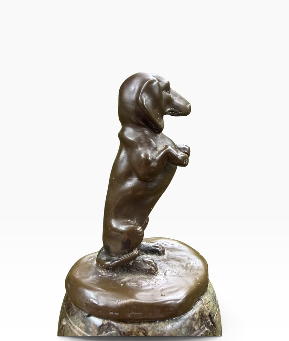 A small dark bronze sculpture of a dachshund standing on its hind legs in a begging position, mounted atop a carved marble barrel base. View V