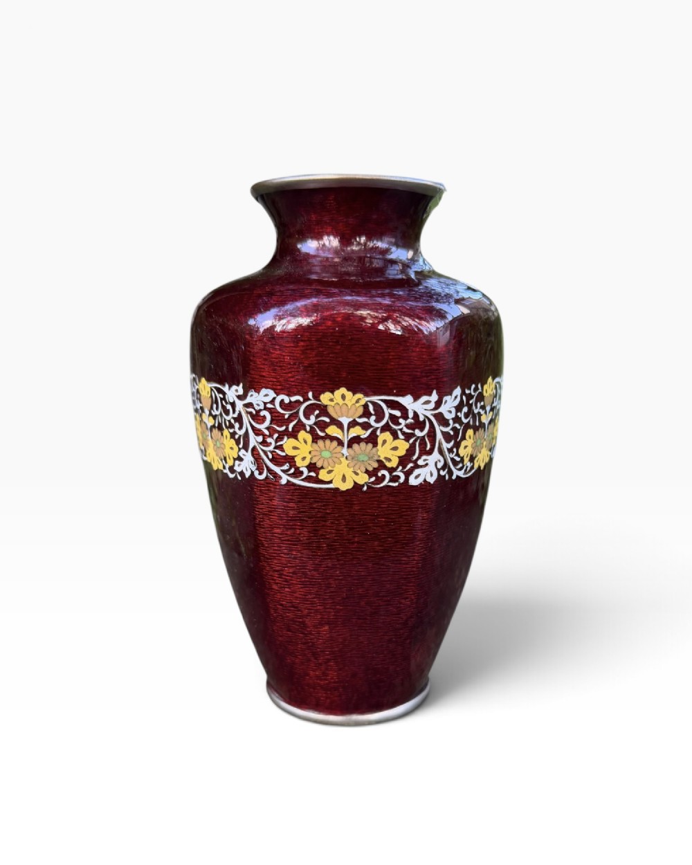 A baluster-shaped Japanese ginbari cloisonne vase featuring deep crimson enamel over foil, decorated with a band of yellow blossoms and white scrolling foliage around the center.