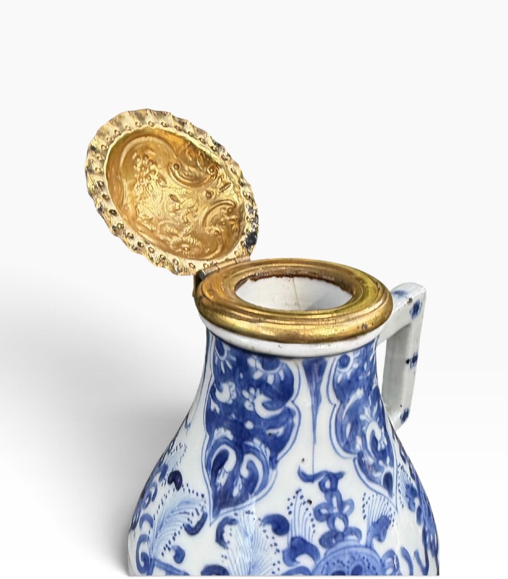A blue and white Kangxi period Chinese porcelain jug with hand-painted floral decoration, an angular ceramic handle, and a chased gilt-metal lid. View V
