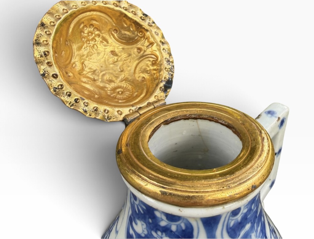 A blue and white Kangxi period Chinese porcelain jug with hand-painted floral decoration, an angular ceramic handle, and a chased gilt-metal lid. View VII
