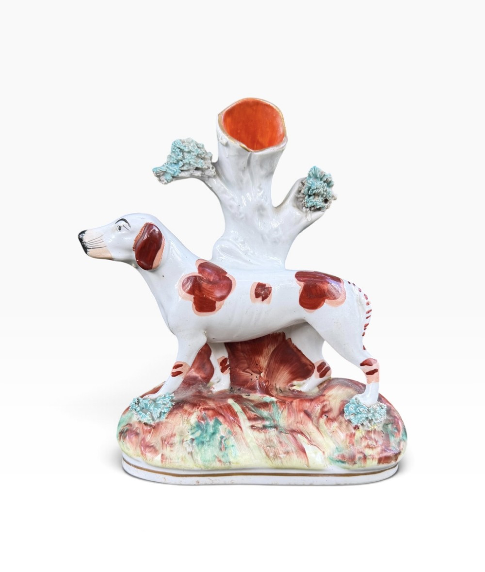 A Victorian Staffordshire pottery spill vase featuring a white and brown pointer dog standing in front of a tree trunk on a moulded base.