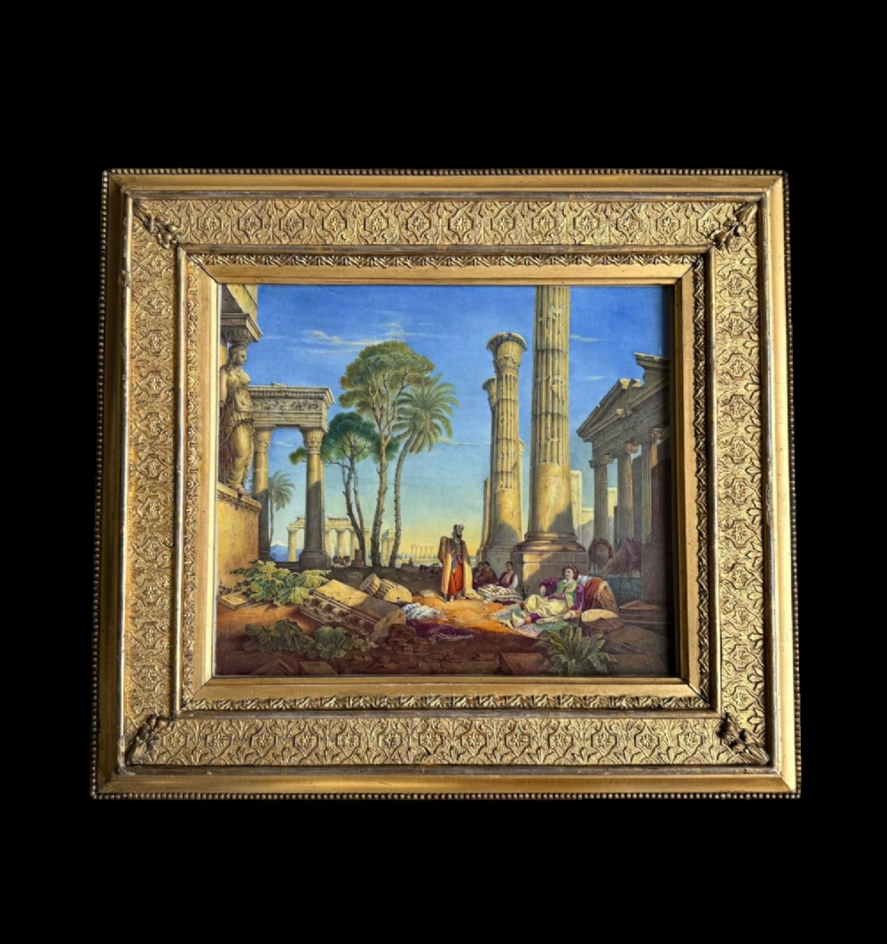 A square hand-painted English porcelain plaque depicting figures among classical ruins, set within a heavily molded gilt frame.