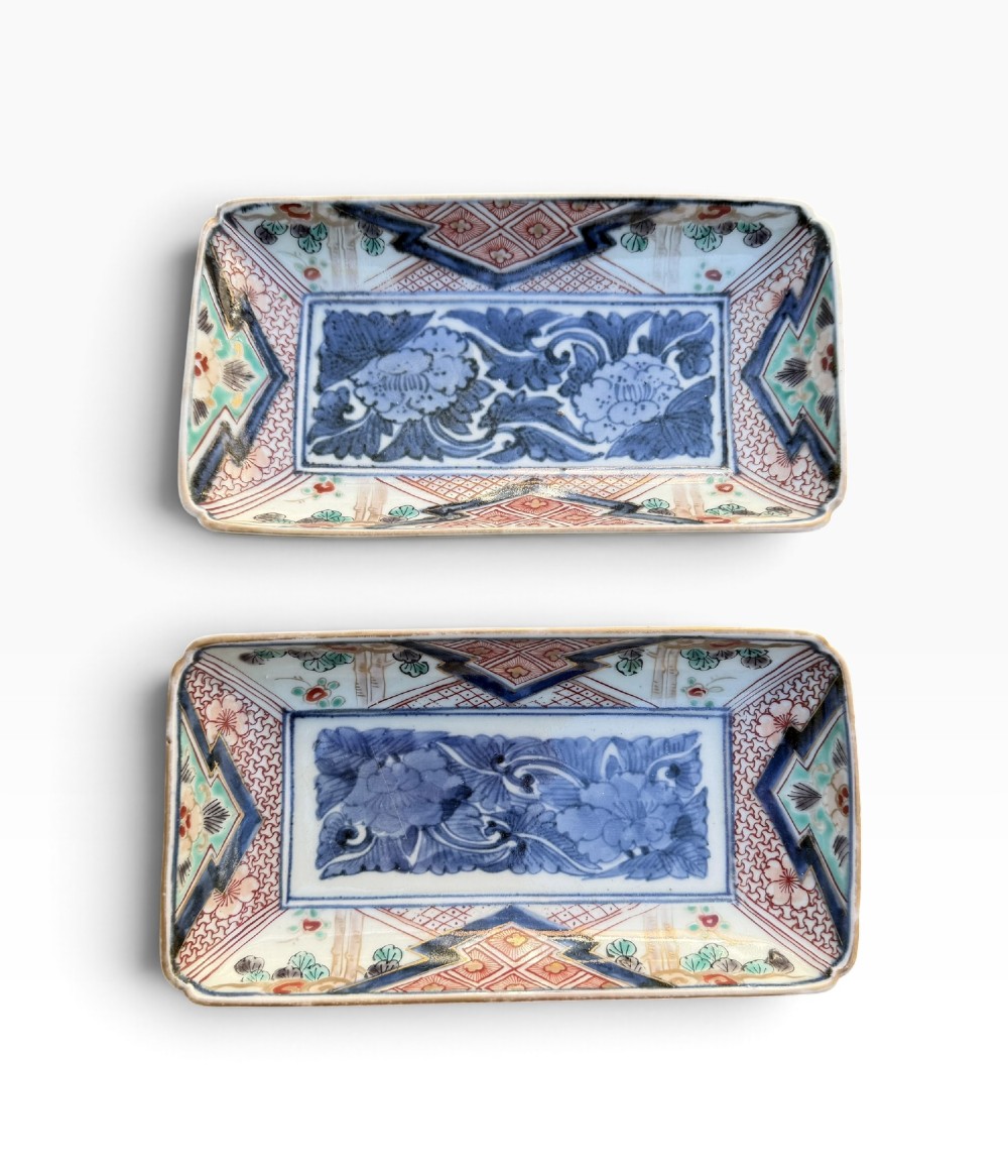 A pair of rectangular Japanese Imari porcelain dishes decorated with central blue floral panels and geometric diaper borders.