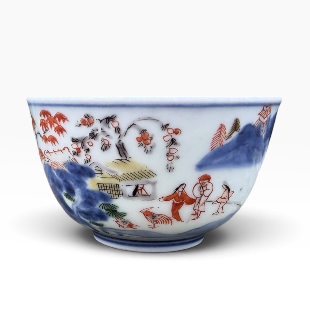 A small Japanese porcelain teabowl decorated with hand-painted figures, foliage, and landscapes in blue, red, green, and yellow enamels.