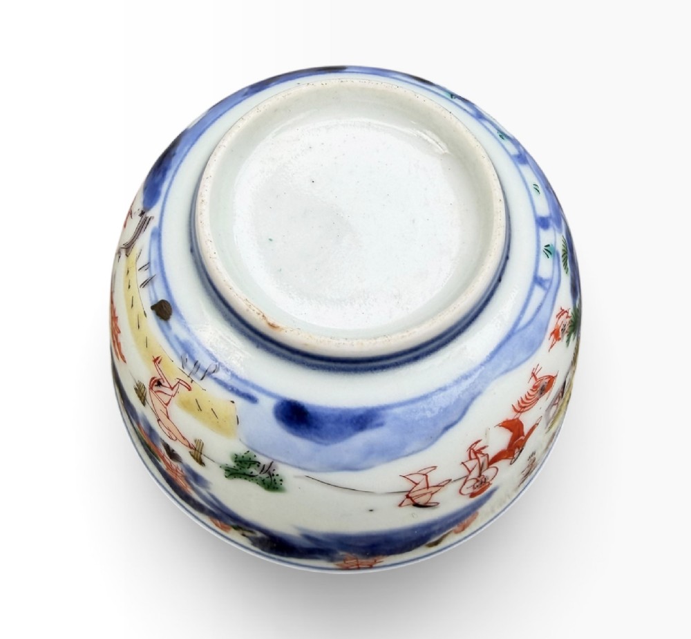 A small Japanese porcelain teabowl decorated with hand-painted figures, foliage, and landscapes in blue, red, green, and yellow enamels. View VII