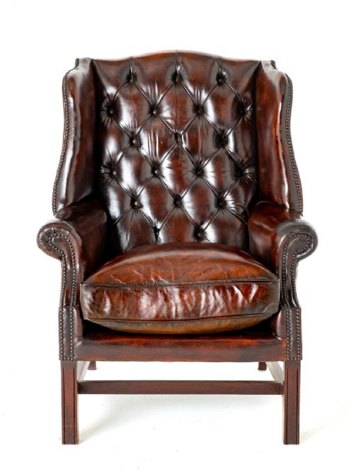 fig 1. A deep chestnut brown leather wingback armchair featuring deep buttoning, brass stud trimming, and square wooden legs with stretchers.