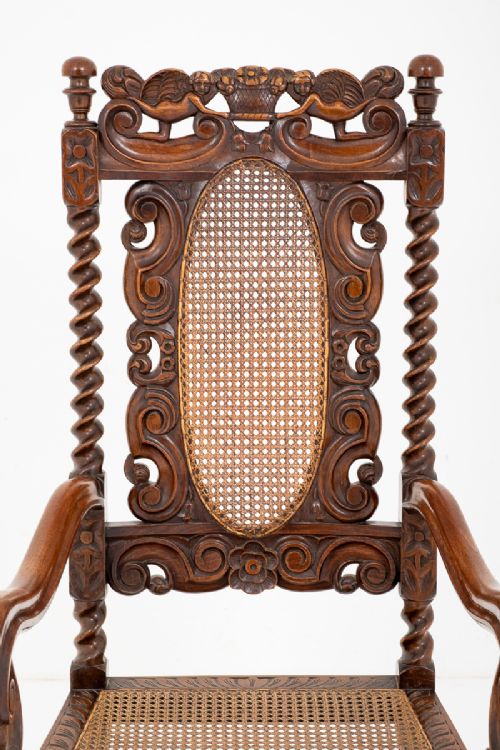 fig 1. A carved oak armchair featuring a woven cane back panel, cane seat, barley twist supports, scrolled arms, and ornate relief carving throughout.