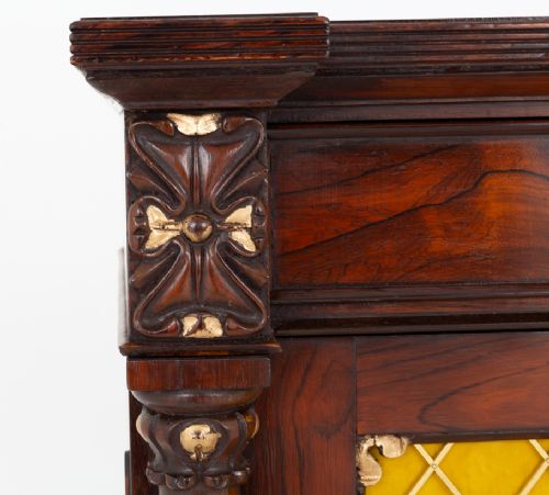 fig 1. A William IV rosewood side cabinet featuring carved columns with gilt details, two upper drawers, and lower doors with brass grilles backed by yellow fabric.