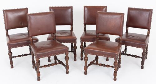 fig 1. A set of six Tudor Revival oak dining chairs with rectangular dark brown leather seats and backs secured by metal studs.