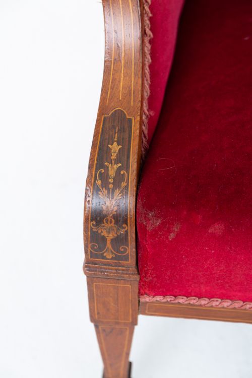 fig 1. An antique Sheraton Revival armchair upholstered in rich crimson red velvet with channelled trim along the back edge, supported on tapered mahogany legs with brass castors.
