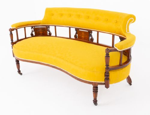 fig 1. An antique curved rosewood settee upholstered in textured yellow fabric, featuring button-backed quilting, turned spindle supports, marquetry inlay panels, and legs on castors.