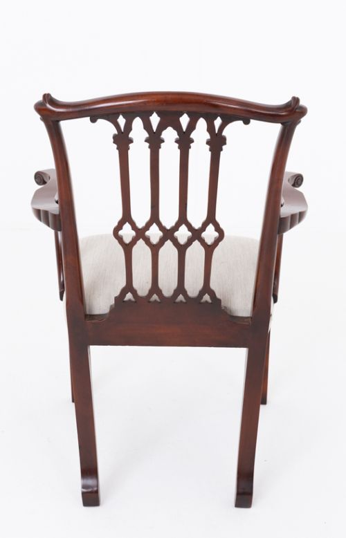 fig 1. A set of twelve carved mahogany dining chairs in the Gothic Revival style, featuring ten side chairs and two carvers with neutral upholstered seats.