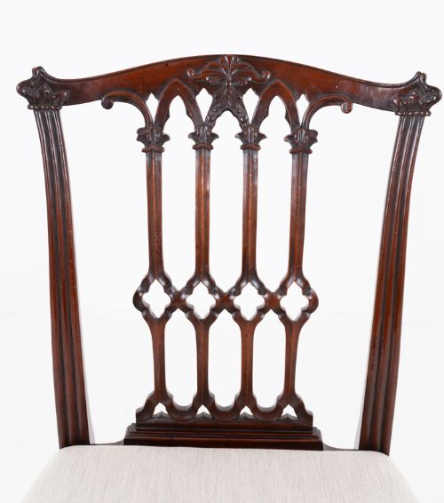 fig 4. A set of twelve carved mahogany dining chairs in the Gothic Revival style, featuring ten side chairs and two carvers with neutral upholstered seats.