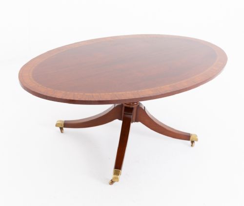fig 2. An oval mahogany coffee table featuring a crossbanded inlaid top, turned central pedestal, four splayed legs, and brass cap castors.