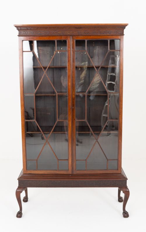 fig 1. A mahogany Chippendale style glazed bookcase featuring geometric glass door panels, a carved frieze, and cabriole legs ending in ball and claw feet.
