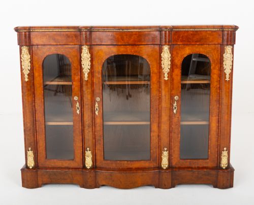 fig 1. A Victorian burr walnut credenza featuring three arched glazed doors, intricate gilt ormolu mounts, and a solid plinth base.