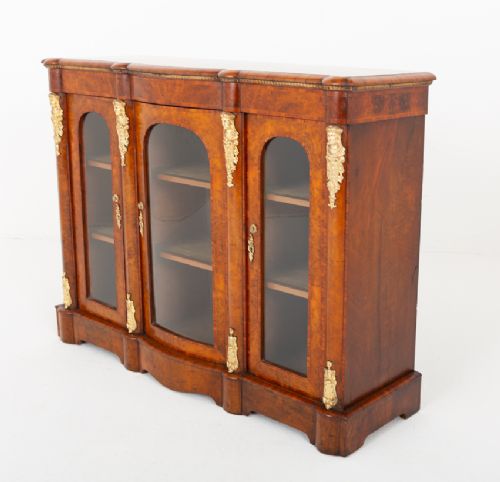 A Victorian burr walnut credenza featuring three arched glazed doors, intricate gilt ormolu mounts, and a solid plinth base. View VIII