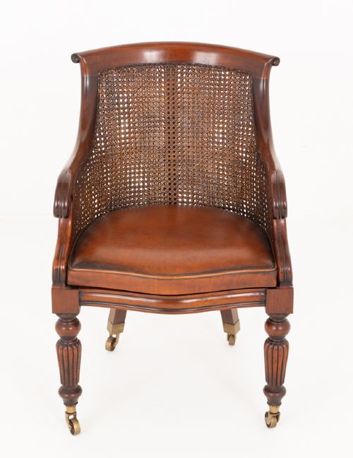 A mahogany Regency Revival desk chair featuring a curved woven cane backrest, a brown leather seat cushion, carved scroll arms, reeded front legs, and brass castors. View II
