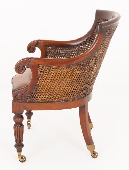 A mahogany Regency Revival desk chair featuring a curved woven cane backrest, a brown leather seat cushion, carved scroll arms, reeded front legs, and brass castors. View III