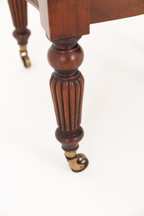 A mahogany Regency Revival desk chair featuring a curved woven cane backrest, a brown leather seat cushion, carved scroll arms, reeded front legs, and brass castors. View IV