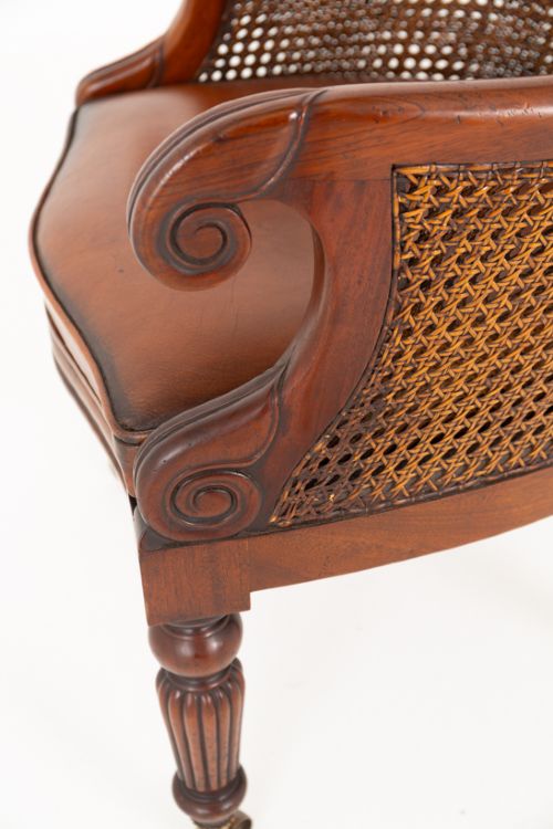 A mahogany Regency Revival desk chair featuring a curved woven cane backrest, a brown leather seat cushion, carved scroll arms, reeded front legs, and brass castors. View VII