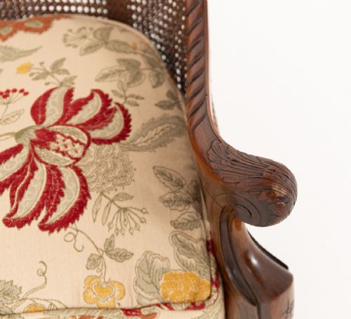 A three-piece Carolean style seating suite comprising a settee and two matching armchairs with woven cane backrests, carved scroll stretchers, and floral fabric seat cushions. View VI